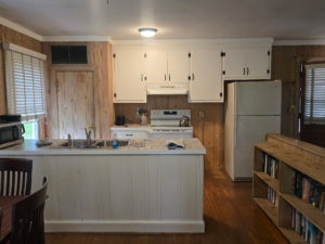 Kitchen with white upper cabinets above a marble-topped island, metal sink, and wood-paneled walls.