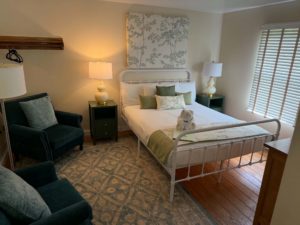 Cozy hotel bedroom with a white metal bed, green throw pillows, and two matching nightstands with lamps.