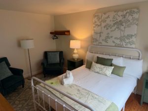 Hotel bedroom with two single beds, botanical-patterned headboard, and a cozy seating area with a lamp and chair on the left.