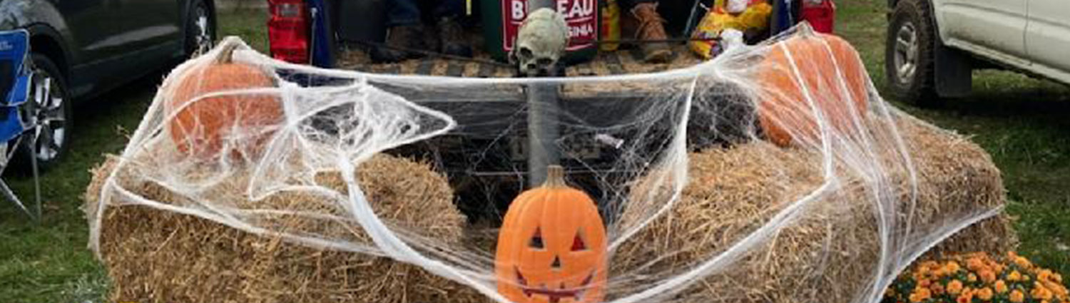 Carved jack-o'-lantern sits on a bale of hay wrapped in fake spider webs for a Halloween display.
